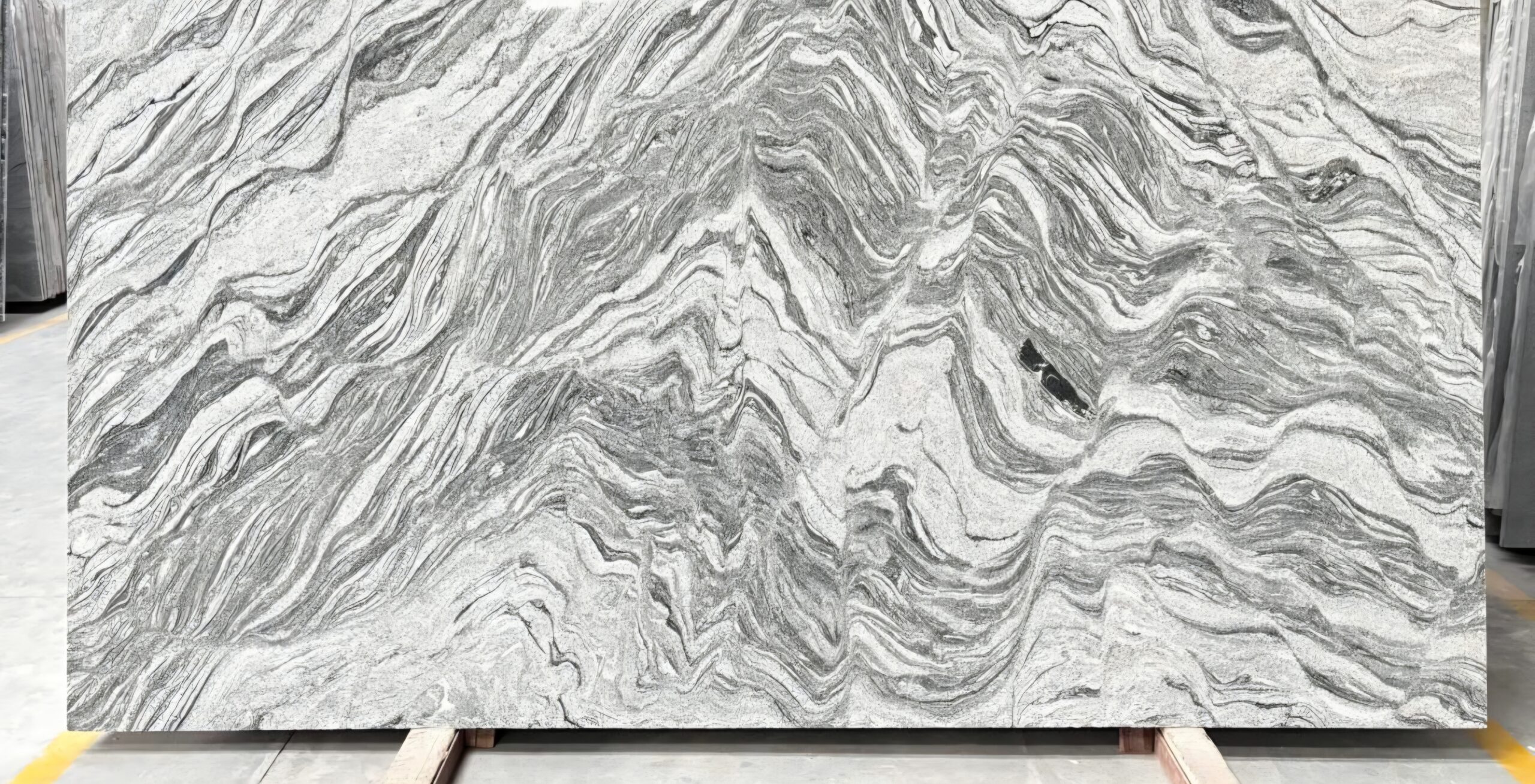 A large quartzite slab with dramatic grey and white folded veining, standing on an A-frame rack in the Pro Granite slab yard