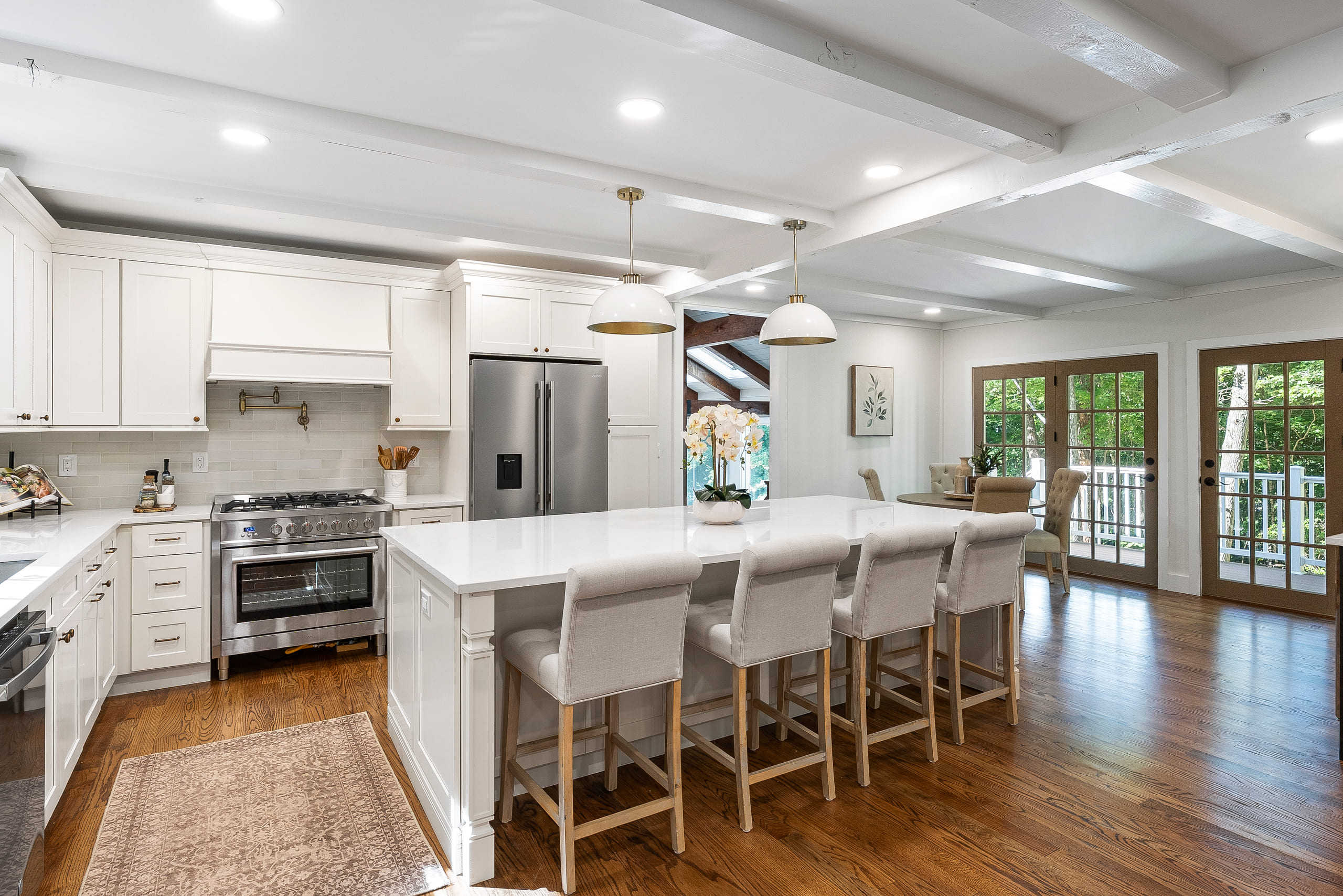 An open white kitchen with a large quartz-topped island, panelled cabinetry, a stainless range under a panelled hood and hardwood flooring, supplied and installed by Pro Granite