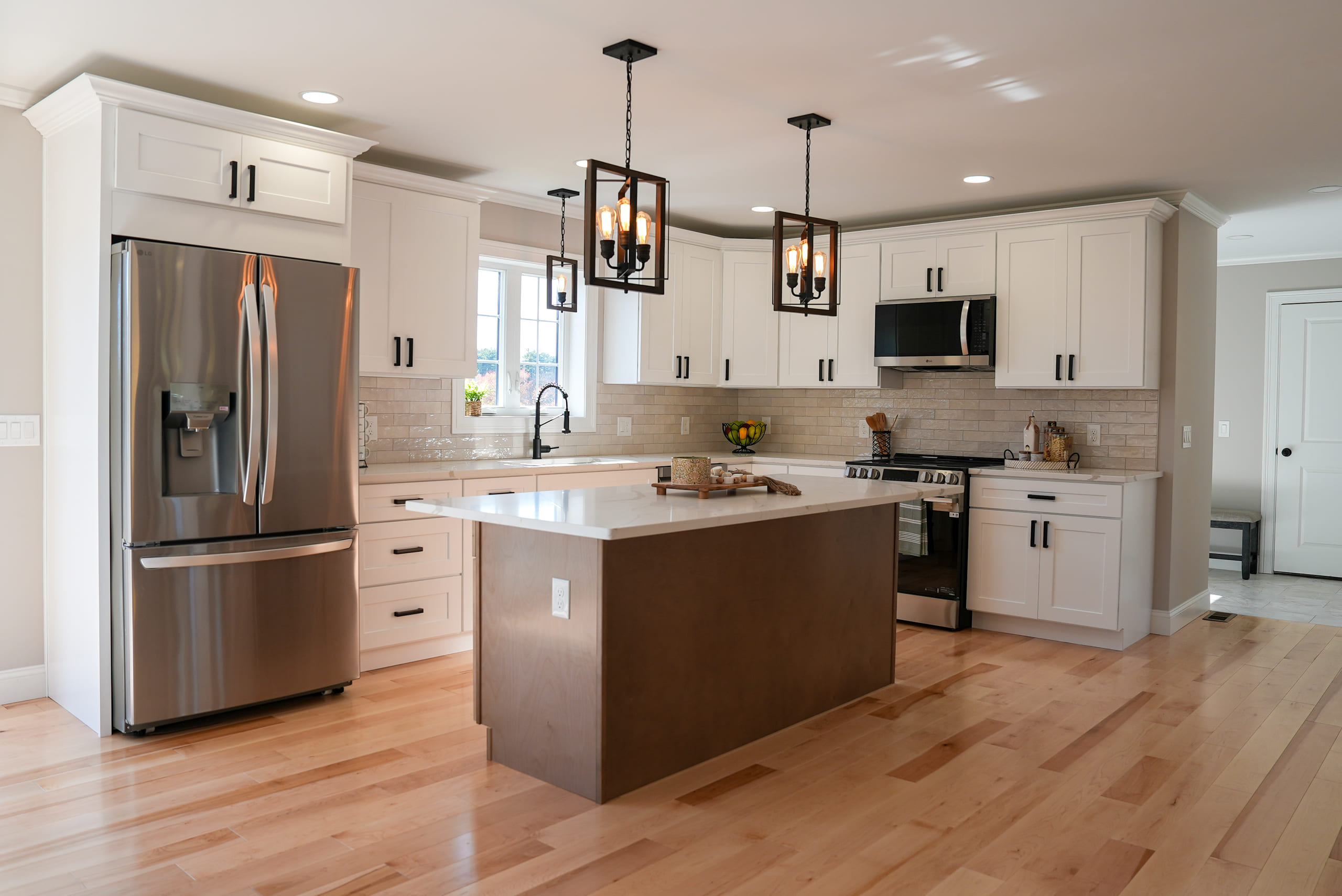 White shaker kitchen with a dark walnut-stained island, two black lantern pendant lights over it, stainless steel appliances and pale maple flooring