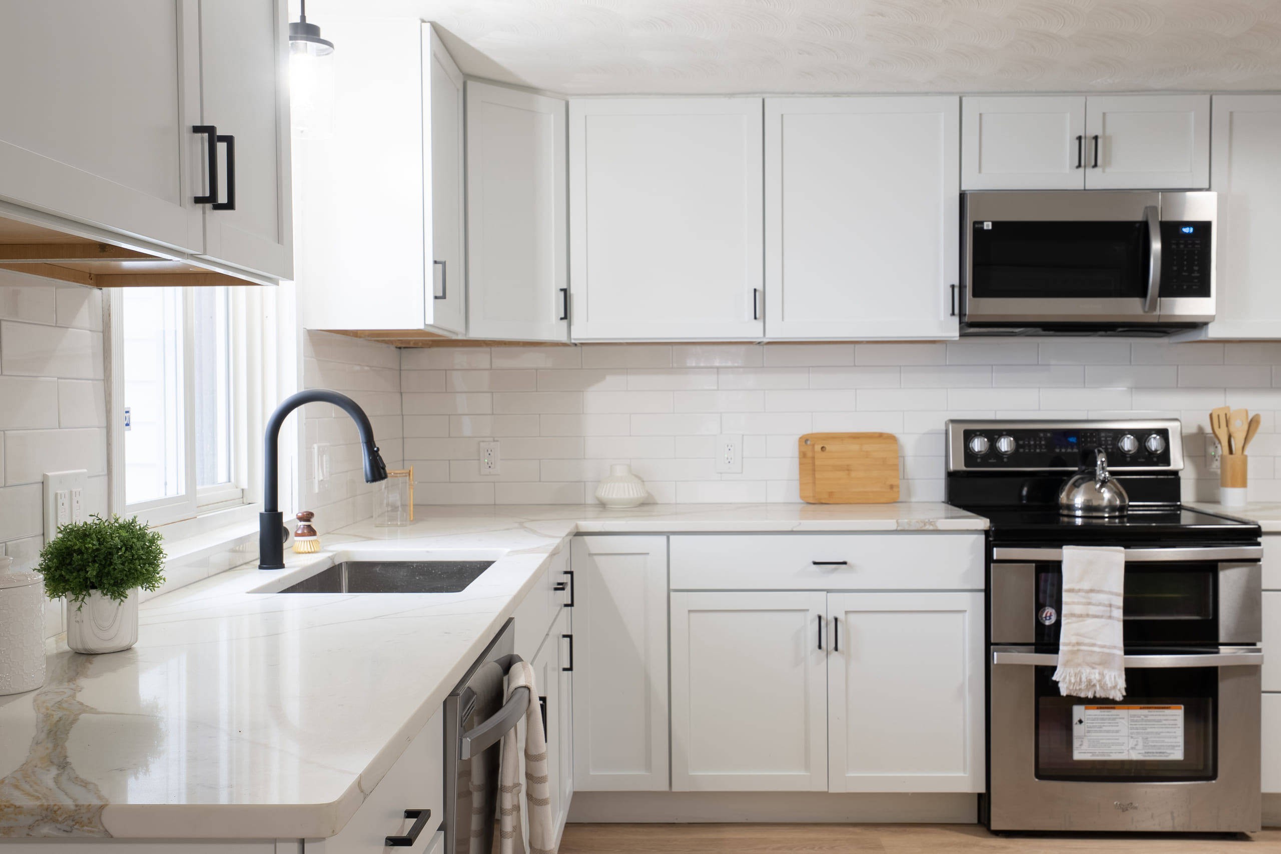 Compact white shaker kitchen with white quartz countertops, a white subway tile backsplash, a matte black gooseneck faucet over an undermount sink and a stainless range with a microwave above it